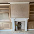 Built-in alcove cupboards with panelled doors and open shelving above on both sides of a fireplace with a carved surround, before painting