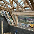 Timber cut roof with rafters and a valley framed over a new blockwork extension, sky visible through the timbers