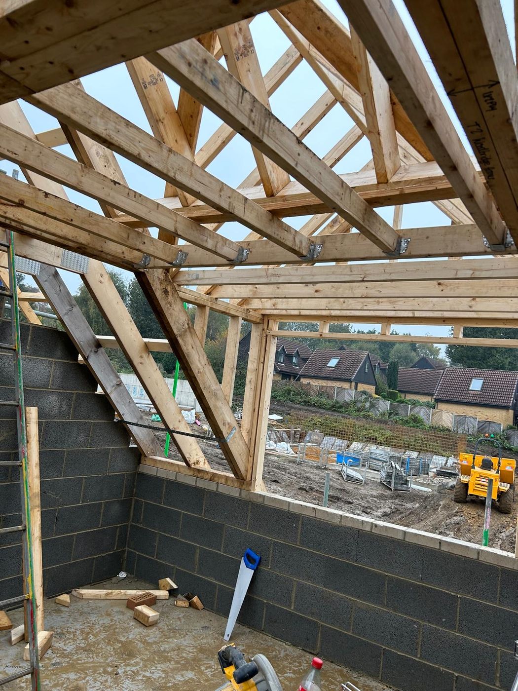 Timber cut roof with rafters and a valley framed over a new blockwork extension, sky visible through the timbers