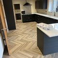 Dark grey shaker kitchen with tall housings, wall units, extractor and an island with a white quartz top on a herringbone floor